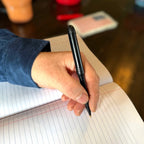 Night black Pokka Pocket Pen being used to write in a notebook